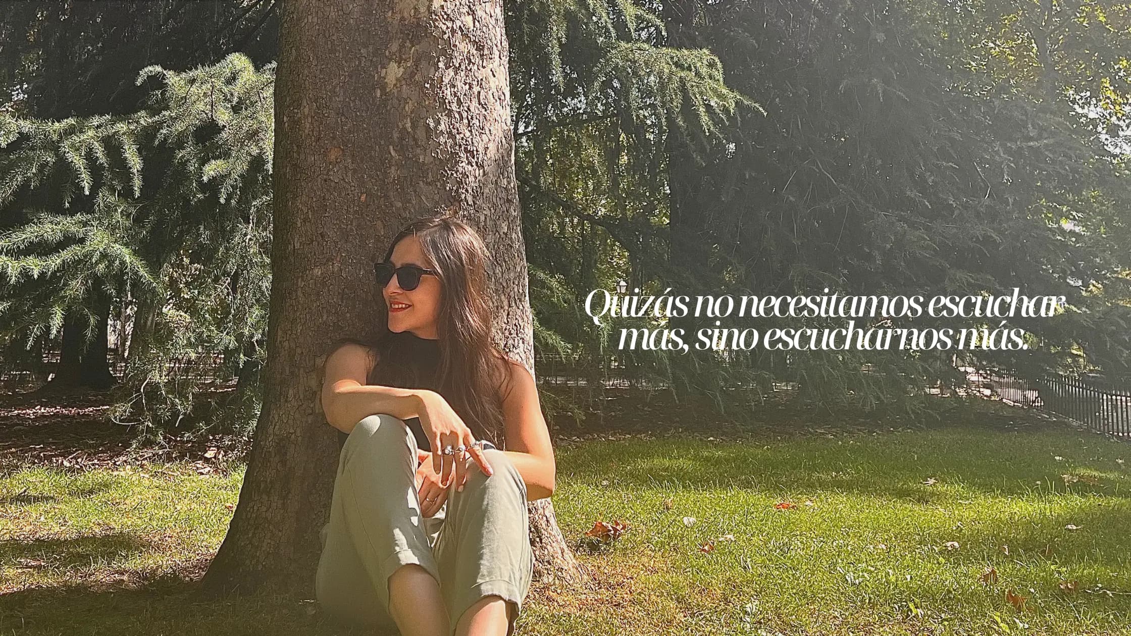 Sandra sentada bajo un árbol en un parque, junto a la frase «Quizás no necesitamos escuchar más, sino escucharnos más»